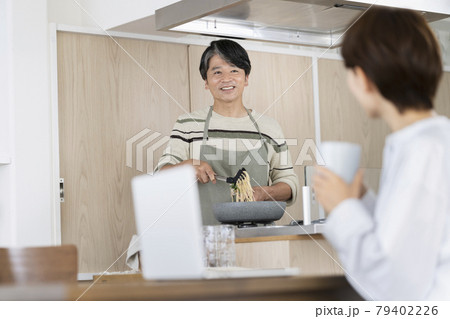 料理をする50代の男性とパソコンで作業する妻　夫婦　イメージ 79402226