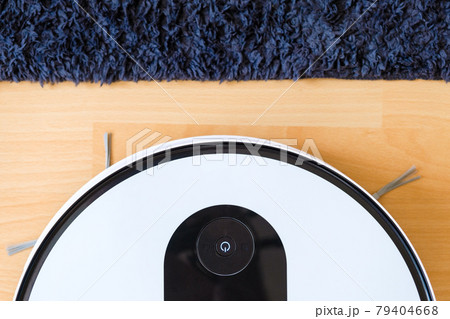 Top view of wireless robot vacuum cleaner cleaning the floor near the carpet and plant 79404668