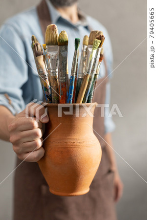 Man artist painter holding clay jug with paint brush. Painter artist and paintbrush in studio 79405665