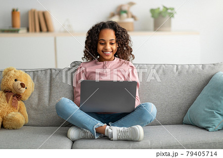 Communication and technology. Smiling black teen girl sitting on sofa and using laptop computer Communication and technology. Smiling black teen girl sitting on sofa and using laptop computer 79405714