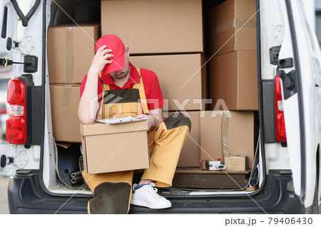 Tired man courier sitting on car with cardboard boxes with documents in his hands 79406430