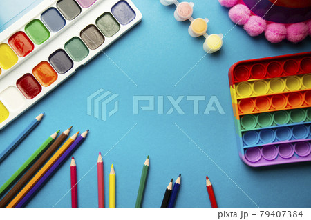 layout top view of children's school items, pop it toy, watercolors, colored pencils on a blue background with place for text 79407384