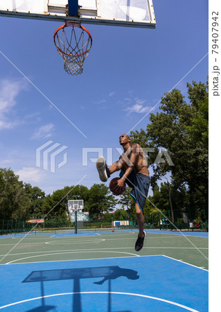 Young man, muscular african male basketball player playing basketball at street public stadium, sport court or palyground outdoors. Summer sport games. 79407942