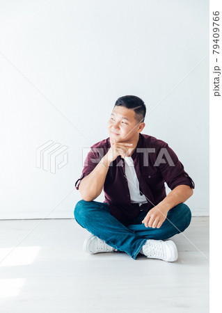 Beautiful Asian man sits on the floor in a white room Beautiful Asian man sits on the floor in a white room 79409766