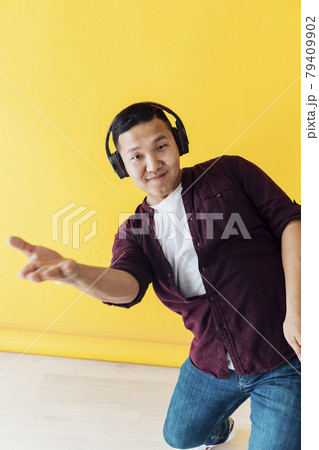 Asian man dances to music with headphones on a yellow background Asian man dances to music with headphones on a yellow background 79409902