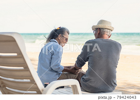 Happy Asian family, senior couple sitting on chairs with backs on beach travel vacation talking together 79424043