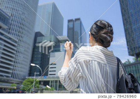 名古屋駅前の高層ビル群を見上げながらカッツポーズしているビジネスウーマン 後ろ姿 79426960