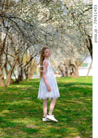 Beautiful blue-eyed girl with blond hair in white dress walking in flower garden,emotional photo. 79431403