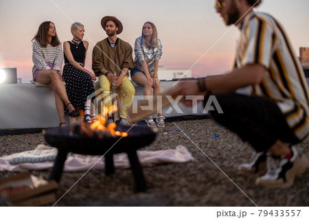Friends by a fireplace on the rooftop at sunset 79433557