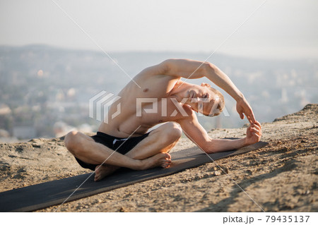 Sportsman doing flexible exercises on yoga mat outdoors Sportsman doing flexible exercises on yoga mat outdoors 79435137