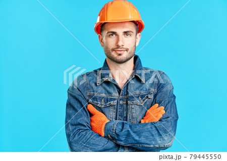 Portrait of confident handsome male construction worker safety helmet with crossed arms over blue background 79445550