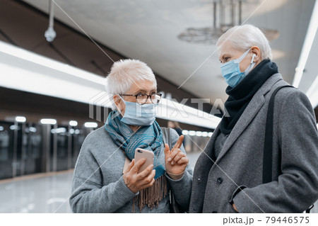 two mature women discussing something while standing on a subway platform. 79446575