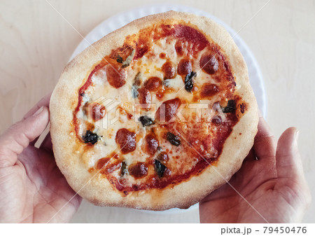 A close-up of a mini pizza in a disposable dish. Top view of takeaway food in fast food cafe. The photo shows mozzarella cheese, tomatoes, olives and various sausages. Meal for one person 79450476