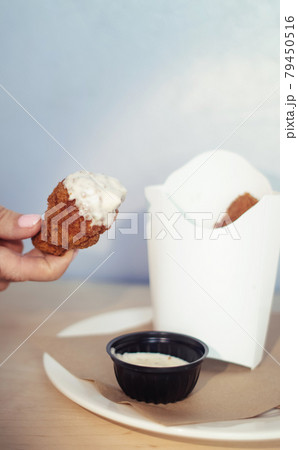 Close-up of chicken wings fried in batter. In a fast food restaurant, there is a cardboard box of chicken and sauce on the table. Sun rays fall beautifully on the hand of the girl who holds the food 79450516