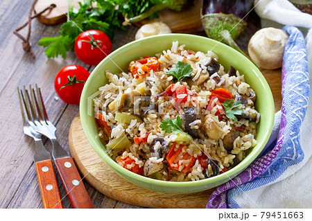 Vegetarian menu, healthy diet food. Rice with vegetables, mushrooms and eggplants in a bowl on a wooden table. 79451663