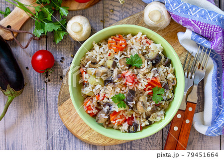 Vegetarian menu, healthy diet food. Rice with vegetables, mushrooms and eggplants in a bowl on a wooden table. Top view of a flat lay with copy space. 79451664