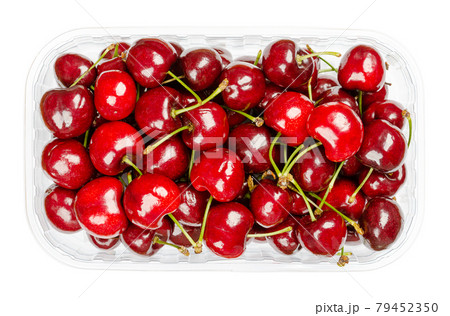 Fresh cherries in a plastic container. Ready to eat, red and ripe fruits of the true cherry species Prunus avium, a stone fruit cultivar. Close-up, from above, isolated, over white, macro food photo. 79452350