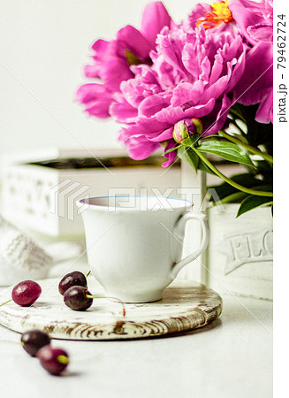 Shabby chic tea. A cup of tea on a white wooden tray with a cherry nearby. Peonies are in a white box. Blurred background 79462724