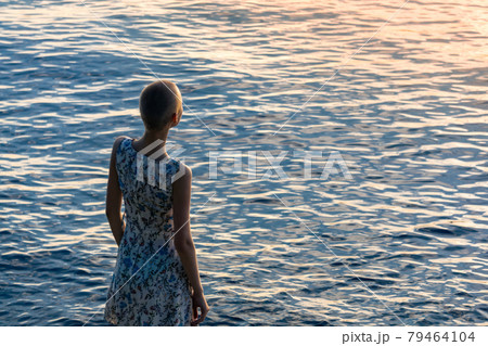 girl teenager in a dress stands on the seashore, looking into the distance girl teenager in a dress stands on the seashore, looking into the distance 79464104