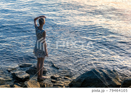 girl teenager in a dress stands on the seashore, looking into the distance girl teenager in a dress stands on the seashore, looking into the distance 79464105