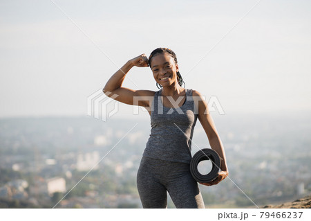 Smiling african woman showing her biceps outdoors Smiling african woman showing her biceps outdoors 79466237