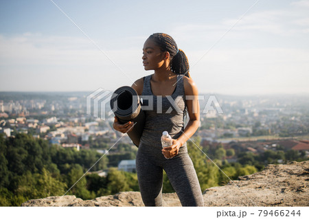 African woman holding yoga mat and bottle of water outdoors 79466244