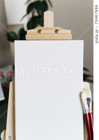 Creative studio. Empty white canvas on a wooden easel and red brushes Creative studio. Empty white canvas on a wooden easel and red brushes 79467686