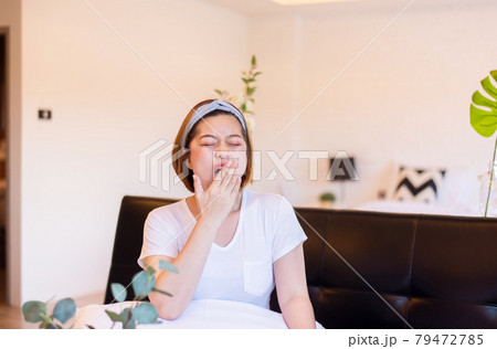 Asian woman yawning covering open mouth with hand sitting on sofa, Tired sleepy,Female with symptoms sleepiness Asian woman yawning covering open mouth with hand sitting on sofa, Tired sleepy,Female with symptoms sleepiness 79472785