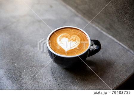 Black cup of cappuccino with latte art of heart shape on saucer on concrete background. Black cup of cappuccino with latte art of heart shape on saucer on concrete background. 79482755