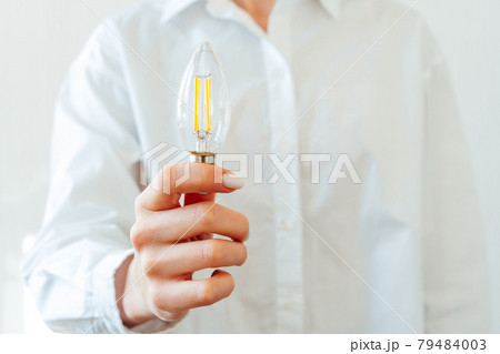 Woman in white shirt holding light bulb in hand 79484003