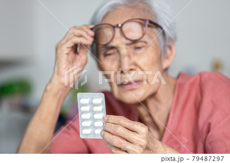 Asian old elderly trying to read medicine label that has small font,problem with very small letters of drug labels or tiny text on products information making her unable to see clearly what is written 79487297