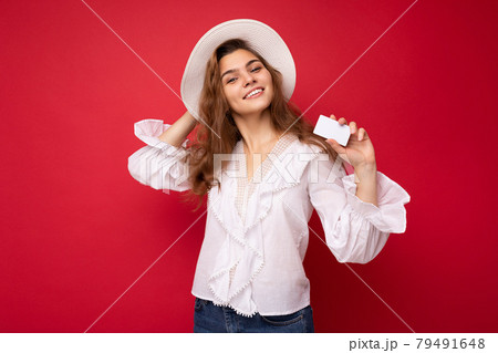 Shot of attractive positive smiling young dark blonde woman wearing white blouse and white hat Shot of attractive positive smiling young dark blonde woman wearing white blouse and white hat 79491648