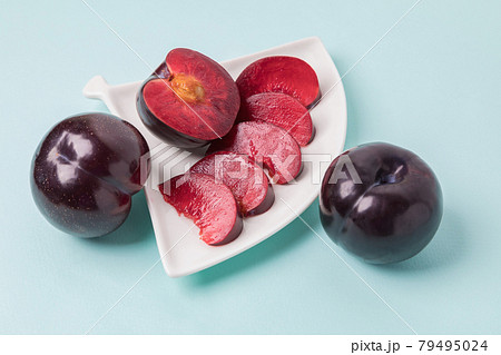 On a white saucer there is a large plum cut into wedges, next to it there are two more plums. 79495024