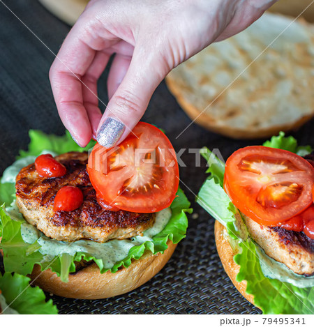 A woman's hand lays down a slice of tomato on a delicious homemade burger. Handmade homemade burgers, close-up A woman's hand lays down a slice of tomato on a delicious homemade burger. Handmade homemade burgers, close-up 79495341