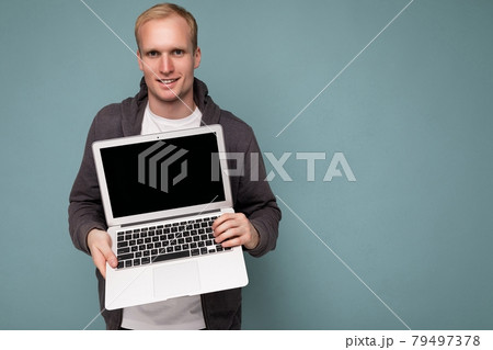 Close-up portrait of handsome blonde man holding computer laptop looking at camera isolated over 79497378