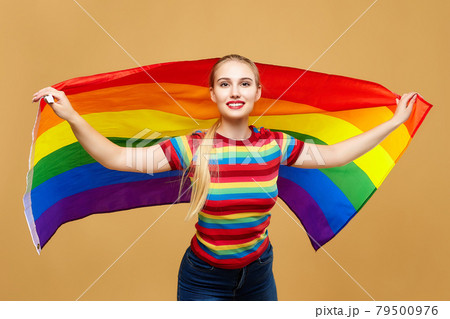 attractive blonde made posing with a rainbow LGBT flag. photo shoot in the studio on a yellow background 79500976
