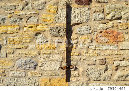 Sturdy yellow and beige cut stone wall and mounted piece of iron 79504465