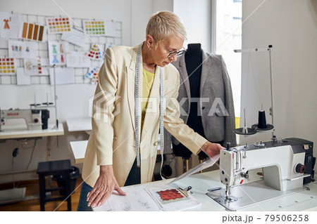 Mature seamstress reads paper at table with modern sewing machine Mature seamstress reads paper at table with modern sewing machine 79506258