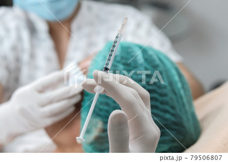 Hand in glove holding botulinum toxin syringe before injection against wrinkles with a nurse assisting. Woman doing anti-aging treatment and face lift in cosmetology clinic. Hand in glove holding botulinum toxin syringe before injection against wrinkles with a nurse assisting. Woman doing anti-aging treatment and face lift in cosmetology clinic. 79506807