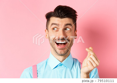 Valentines day concept. Romantic guy showing finger heart and looking left, smiling happy, standing on pink background dreamy 79510111