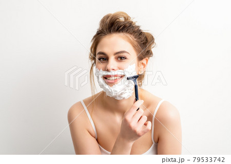Portrait of beautiful young smiling caucasian woman shaves face with razor on white background. 79533742