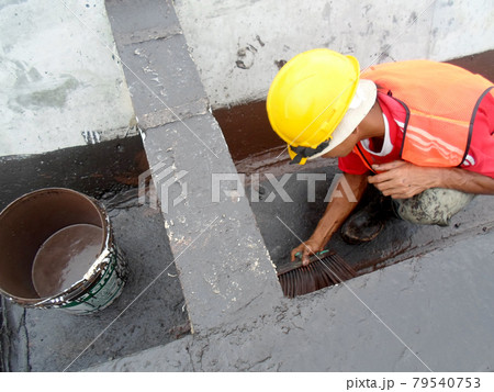 SELANGOR, MALAYSIA -SEPTEMBER 16, 2014: Construction worker apply layers of bituminous waterproofing at the building roof slab surface. SELANGOR, MALAYSIA -SEPTEMBER 16, 2014: Construction worker apply layers of bituminous waterproofing at the building roof slab surface. 79540753