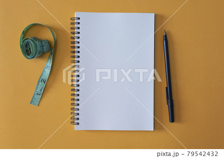 Notepad with pen and measurement tap on yellow background Notepad with pen and measurement tap on yellow background 79542432
