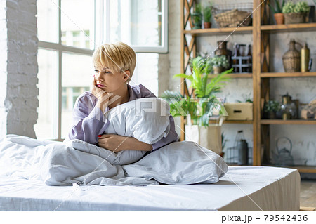 Photo of a sad woman sitting on the bed in the morning. she sits hugging her pillow. She didn't get enough sleep. Photo of a sad woman sitting on the bed in the morning. she sits hugging her pillow. She didn't get enough sleep. 79542436