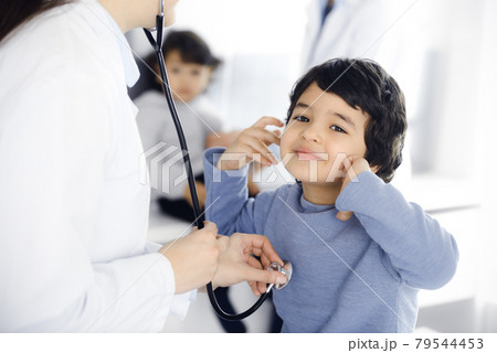 Doctor-woman examining a child patient by stethoscope. Cute arab boy and his brother at physician appointment. Medicine concept 79544453