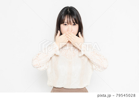 白背景の前に立って、口を隠す、レースのブラウスを着た若い女性 79545028