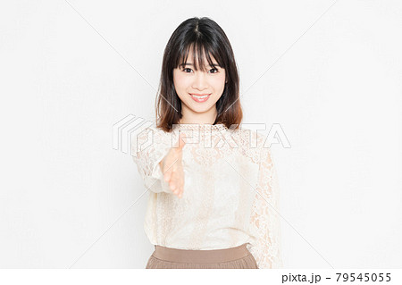 白背景の前に立って、握手のジェスチャーをする、レースのブラウスを着た若い女性 79545055
