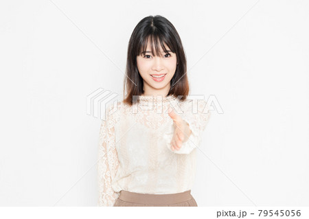 白背景の前に立って、握手のジェスチャーをする、レースのブラウスを着た若い女性 79545056