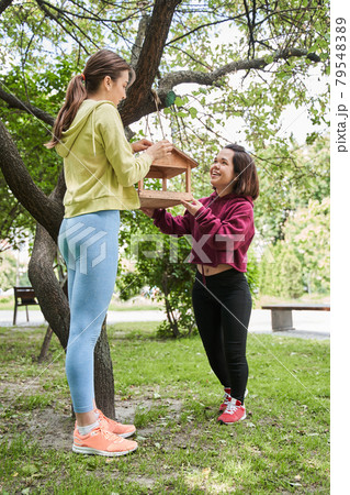 Midget woman adjusting birds feeder at the tree with her best friend Midget woman adjusting birds feeder at the tree with her best friend 79548389