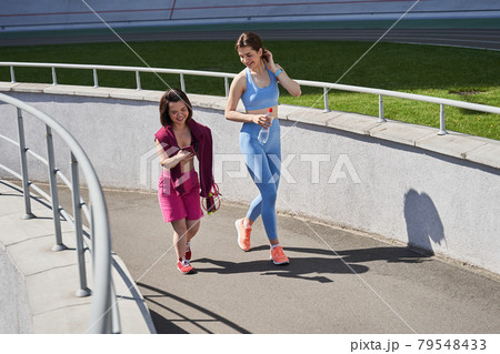 Girl walking through the stadium track with her best friend after running Girl walking through the stadium track with her best friend after running 79548433
